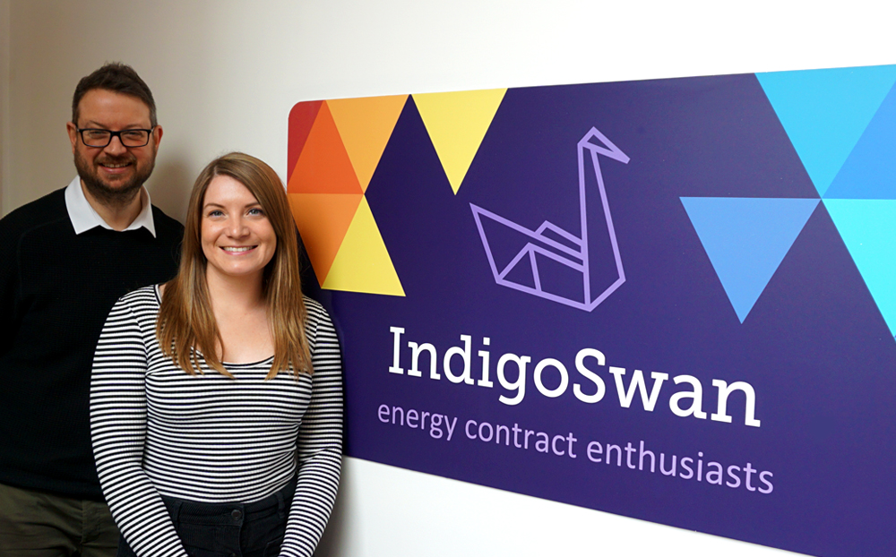 Hayley and James standing in front of Indigo Swan sign|Hayley and James sitting on the sofa reading books|Business values on the wall|Pictures in frames on the wall|Hayley and James standing in front of Indigo Swan sign|Business values on the wall|Hayley and James standing in front of Indigo Swan sign|New Anglia Logo