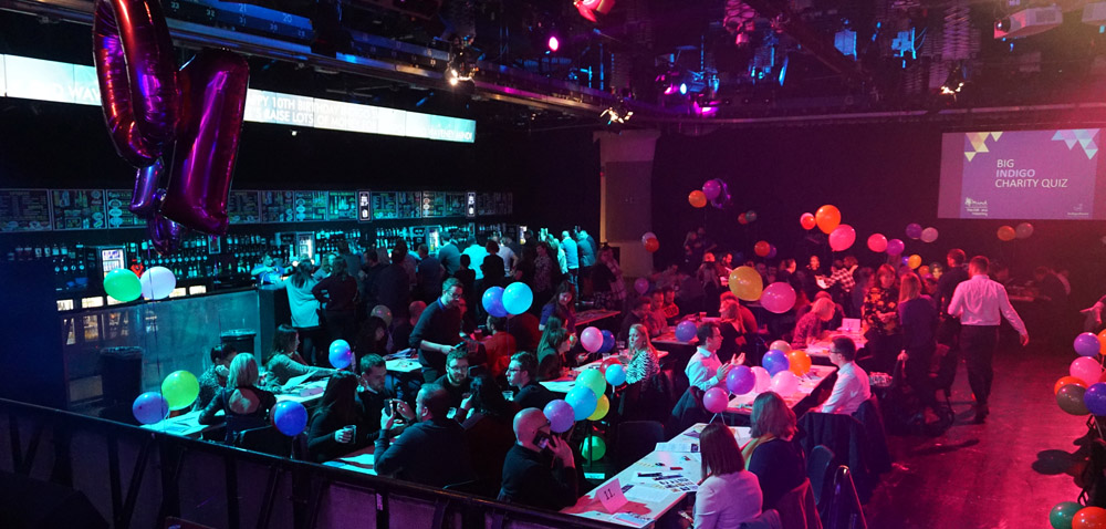 Room full of people sitting at tables taking part in a quiz|||People standing on chairs building towers||Collection of photos||